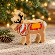 Wooden reindeer toy beneath Christmas tree branches beside a pinecone and warm fairy lights