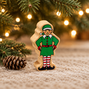 Wooden elf toy beneath Christmas tree branches beside a pinecone and warm fairy lights