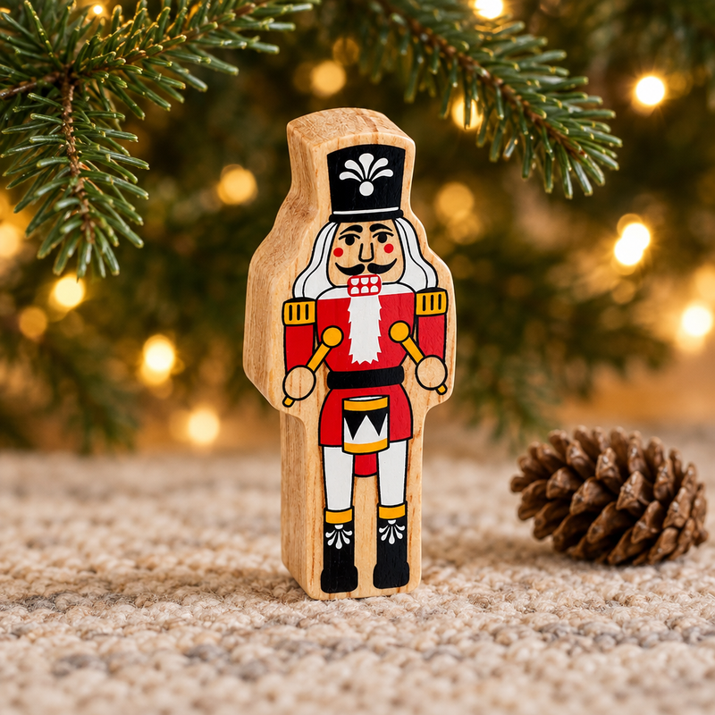 Wooden nutcracker toy beneath Christmas tree branches beside a pinecone and warm fairy lights