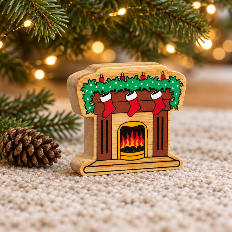 Wooden fireplace toy with stockings beneath Christmas tree branches beside a pinecone and warm fairy lights