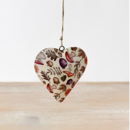 Cream metal hanging heart with autumnal botanical print featuring oak leaves, acorns, berries, mushrooms and seed pods in muted tones, hung on jute twine, wooden surface background