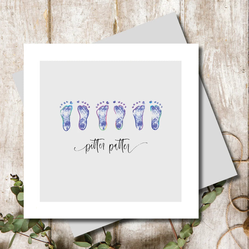 New baby boy card with three pairs of tiny rainbow foil baby footprints on a soft grey background with pitter patter sentiment in handwritten script, 155 x 155mm