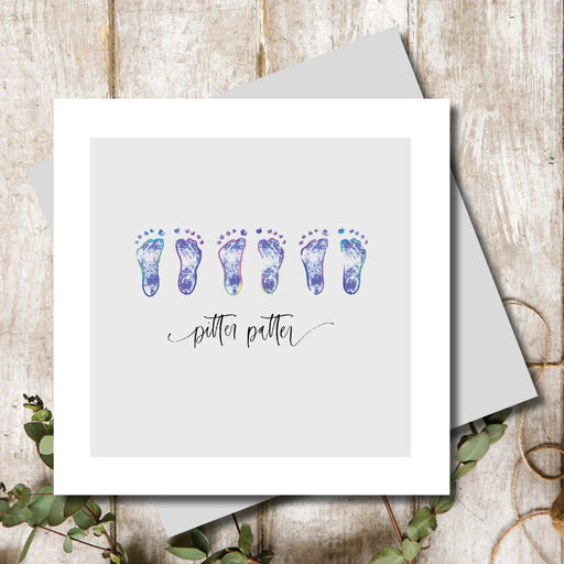 New baby boy card with three pairs of tiny rainbow foil baby footprints on a soft grey background with pitter patter sentiment in handwritten script, 155 x 155mm