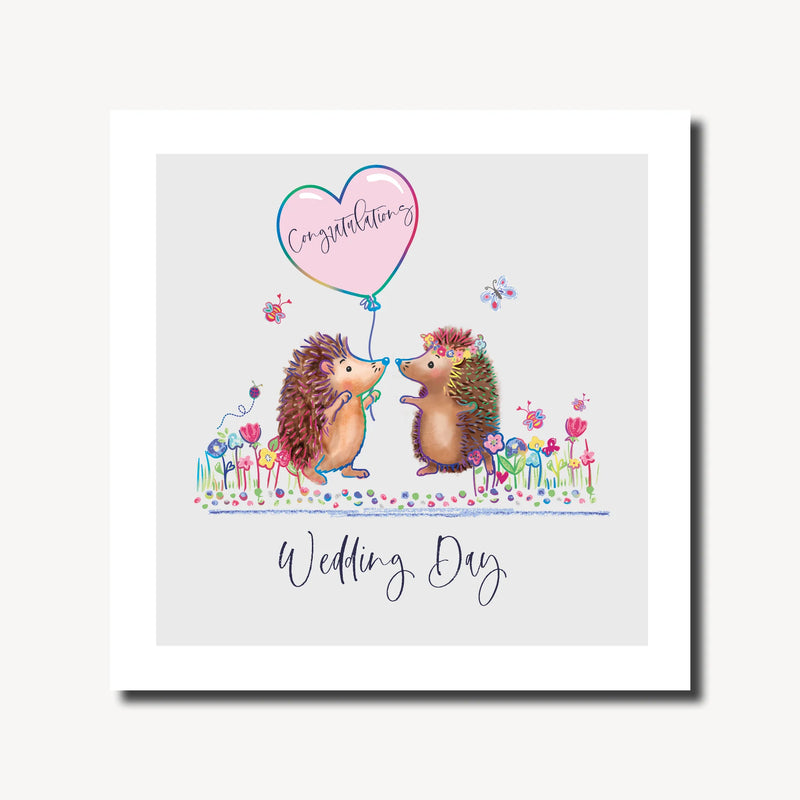 Wedding day card with two illustrated hedgehogs facing each other, one holding a pink heart Congratulations balloon and one wearing a floral crown, among colourful wildflowers, rainbow foil finish, 6.1 x 6.1 inches⠋