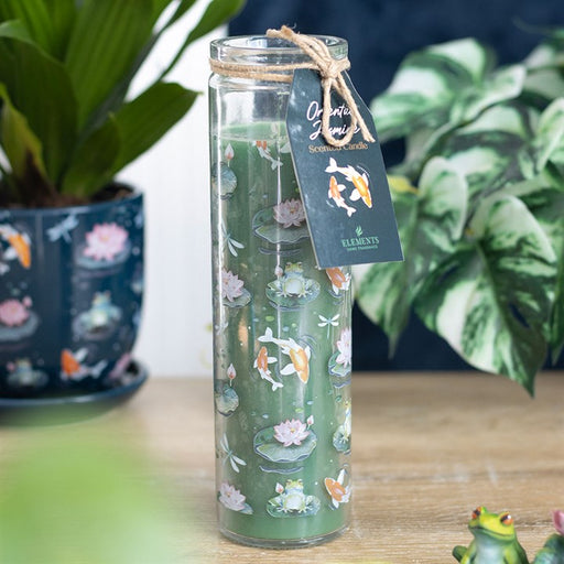 Pond Print Oriental Jasmine tube candle in glass jar with green twine bow, lit and styled with pond-themed ornaments in the background