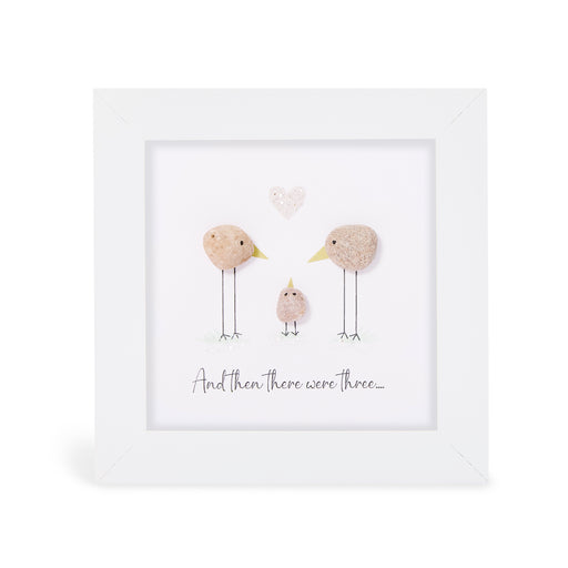 Pebble art framed plaque with two natural pebble birds facing each other with a tiny pebble chick between them and a small heart pebble above, with the sentiment "And then there were three...", white frame