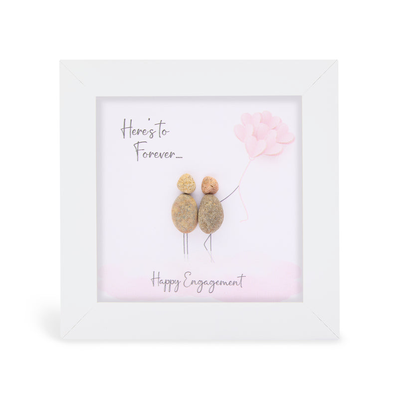 Pebble art framed plaque with two natural pebble figures standing together, one holding pink heart-shaped balloons, and the sentiments "Here's to Forever..." and "Happy Engagement", white frame