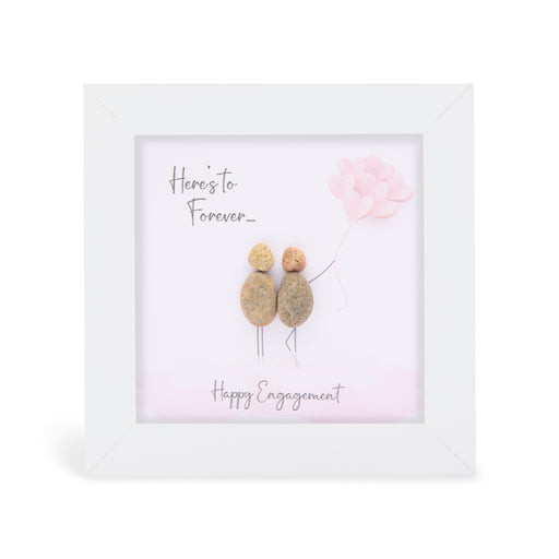Pebble art framed plaque with two natural pebble figures standing together, one holding pink heart-shaped balloons, and the sentiments "Here's to Forever..." and "Happy Engagement", white frame