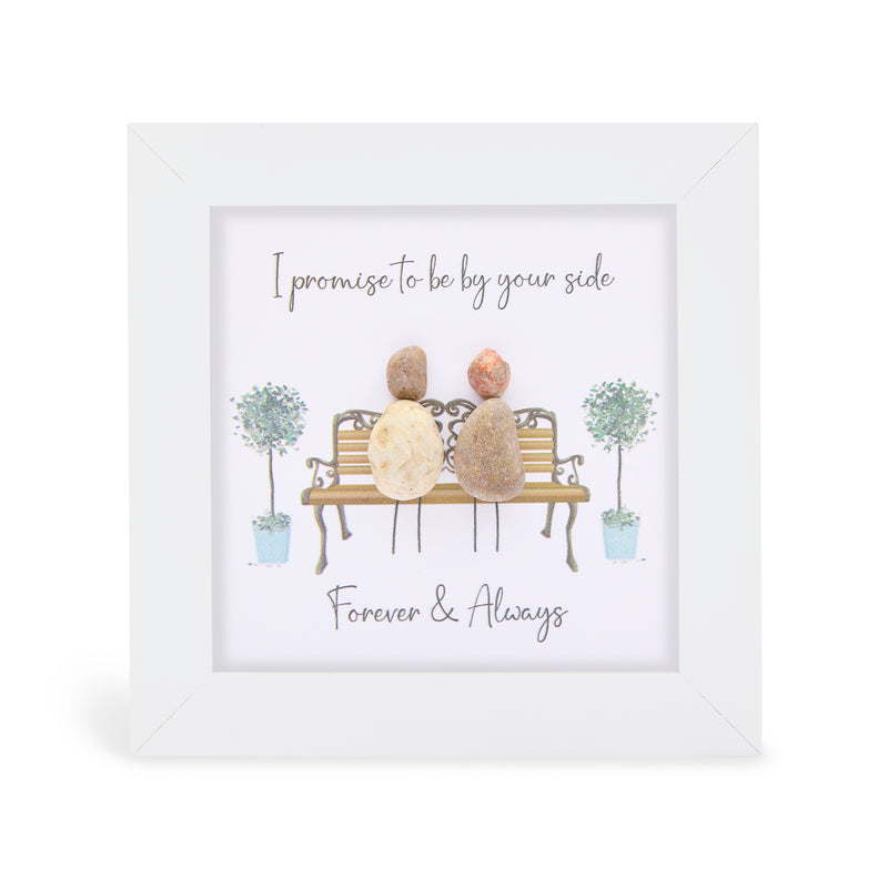 Pebble art framed plaque with two natural pebble figures sitting on an ornate bench flanked by illustrated topiary trees, with the sentiments "I promise to be by your side" and "Forever & Always", white frame