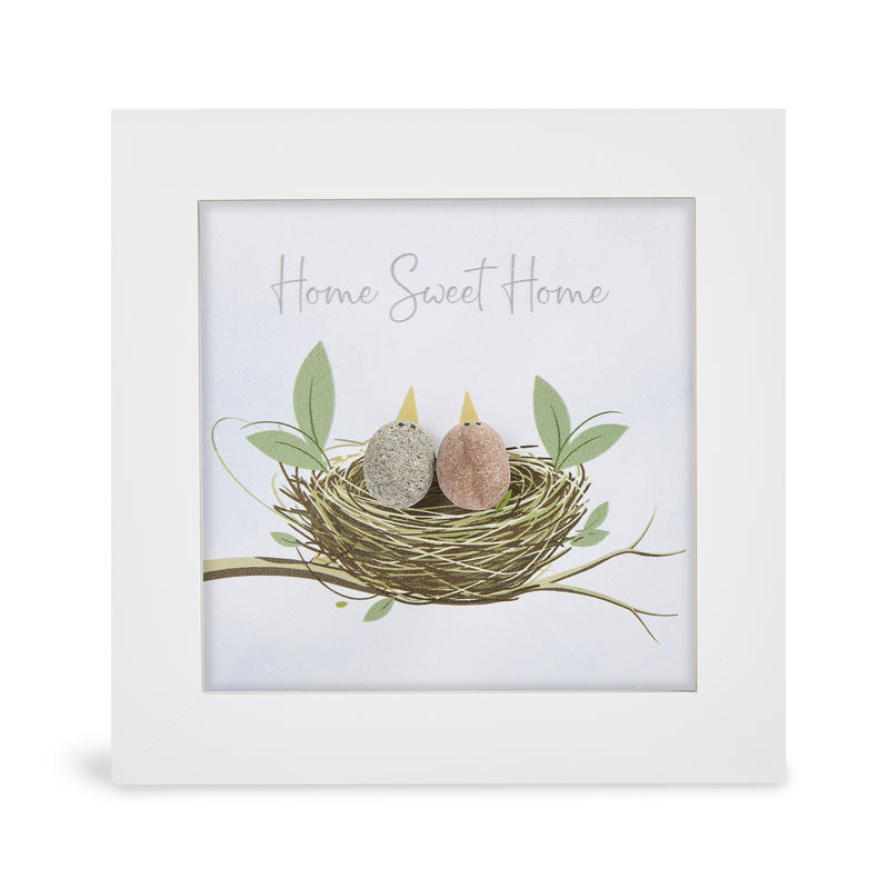 Pebble art framed plaque with two natural pebble birds with yellow beaks nestled together in an illustrated nest on a branch with green leaves and the sentiment "Home Sweet Home", white frame