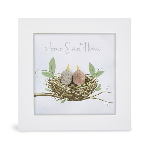 Pebble art framed plaque with two natural pebble birds with yellow beaks nestled together in an illustrated nest on a branch with green leaves and the sentiment "Home Sweet Home", white frame