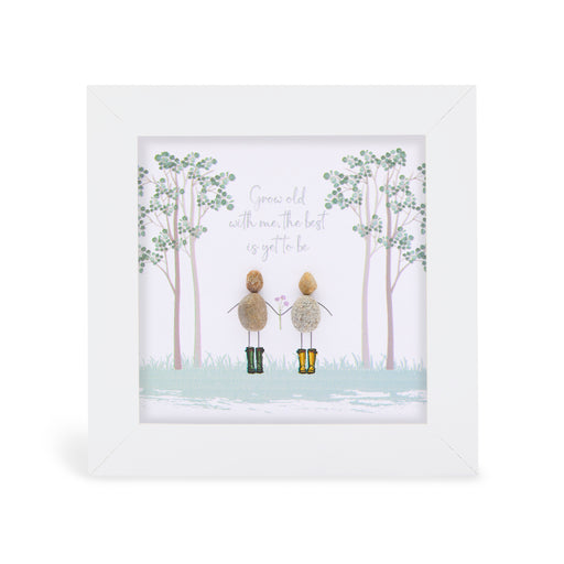 Pebble art framed plaque with two natural pebble figures standing hand in hand in a misty woodland scene, one in dark green wellies and one in yellow wellies holding a small flower, with the sentiment "Grow old with me, the best is yet to be", white frame