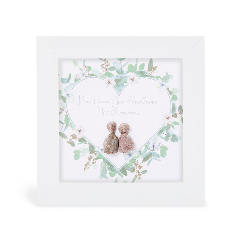 Pebble art framed plaque with two natural pebble figures inside an illustrated heart wreath of soft green foliage, white flowers and butterflies, with the sentiment "New Home, New Adventures, New Memories", white frame