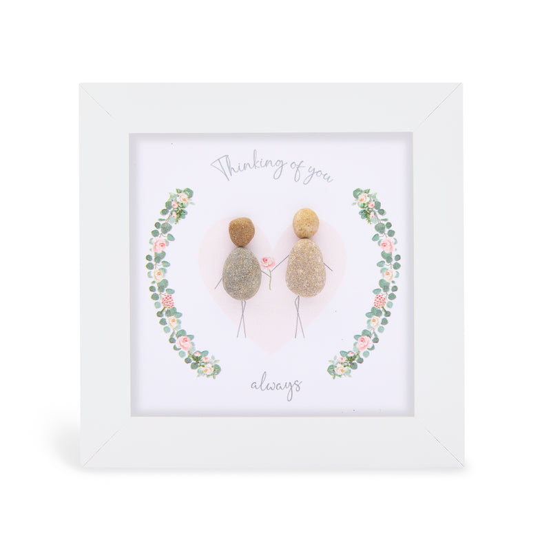 Pebble art framed plaque with two natural pebble figures holding a flower inside an illustrated floral wreath and the sentiment "Thinking of you always", white frame