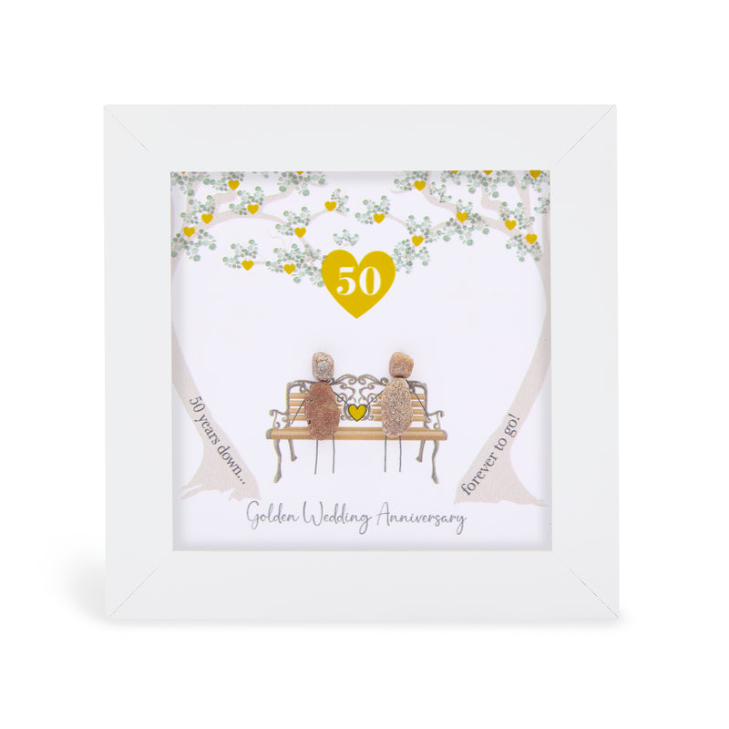 Pebble art framed plaque with two natural pebble figures on an ornate bench beneath a tree with gold hearts, a gold heart with the number 50 above them, and the sentiment "50 years down... forever to go! Golden Wedding Anniversary", white frame