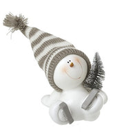 Sitting skating snowman decoration with grey striped bobble hat, ice skates and miniature snow-dusted Christmas tree, without scarf
