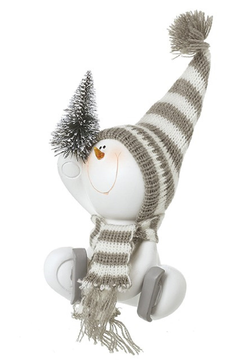 Sitting skating snowman decoration with grey striped bobble hat, knitted scarf, ice skates and miniature snow-dusted Christmas tree held aloft
