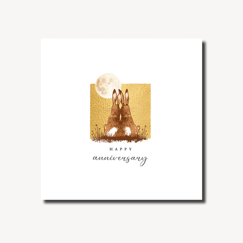 Happy anniversary card featuring two hares sitting side by side in a moonlit meadow with a full moon and warm gold foil background, blank inside, square format 155 x 155mm