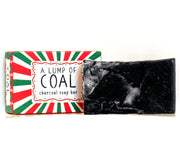 Neon Magpie Christmas Lump of Coal Vegan Soap Bar in red and green striped festive packaging with sunburst design, with dark charcoal soap bar shown alongside
