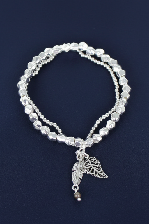 Silver plated two-strand elasticated bracelet with nugget beads, small round beads and three leaf charms on a deep navy blue background