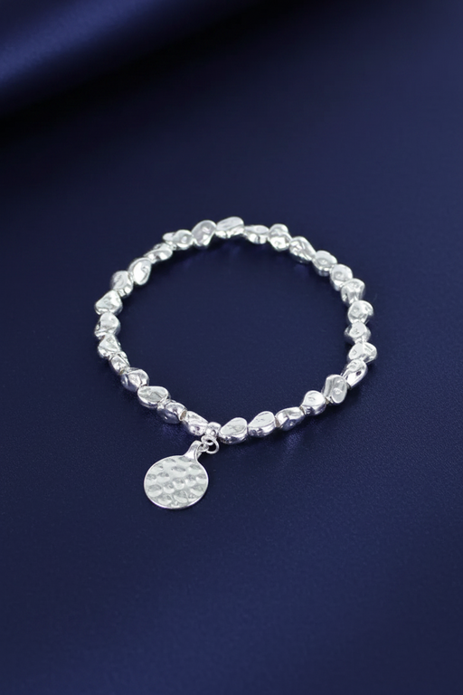 Silver plated nugget bead elasticated bracelet with a disc charm on a deep navy blue background