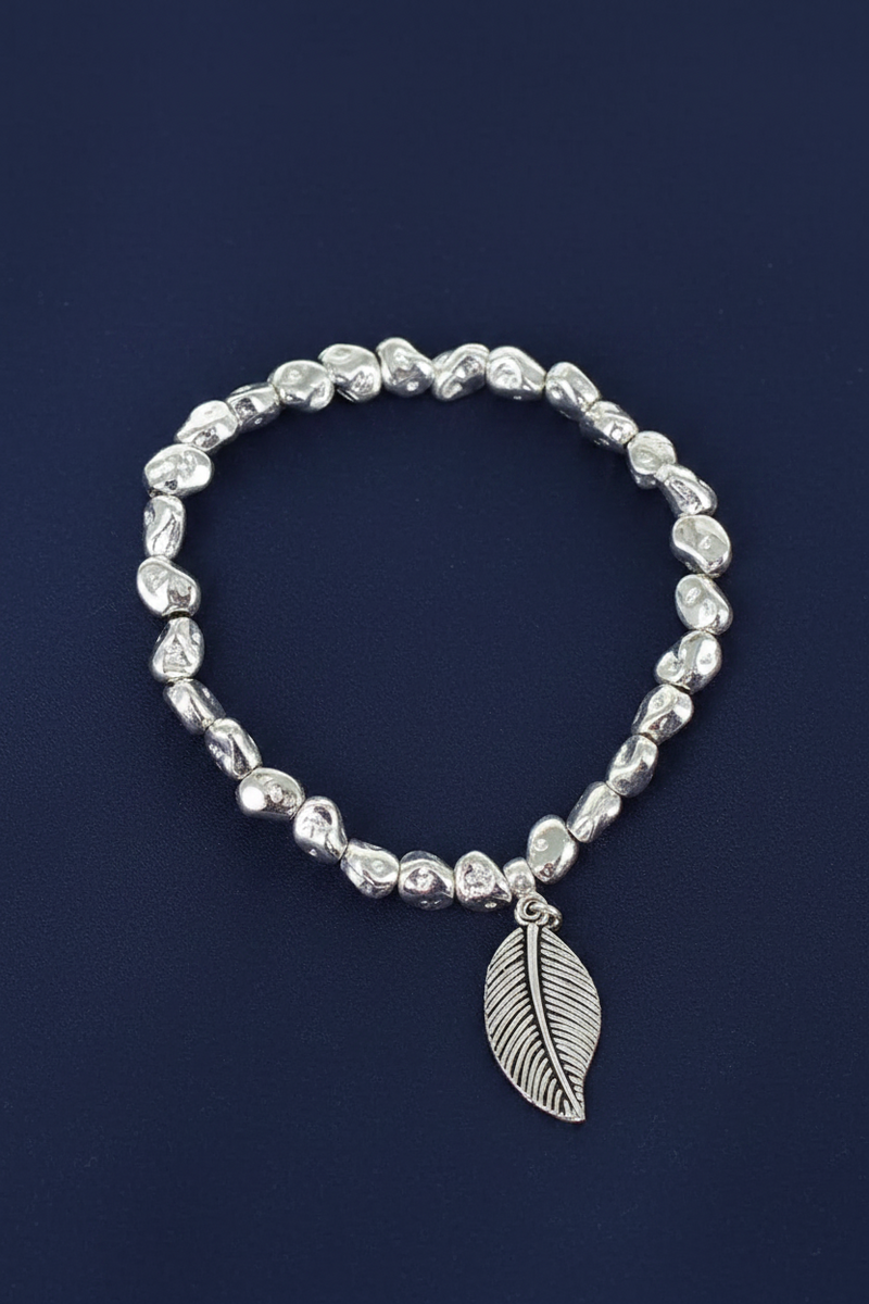 Silver plated nugget bead elasticated bracelet with a finely textured leaf charm on a deep navy blue background