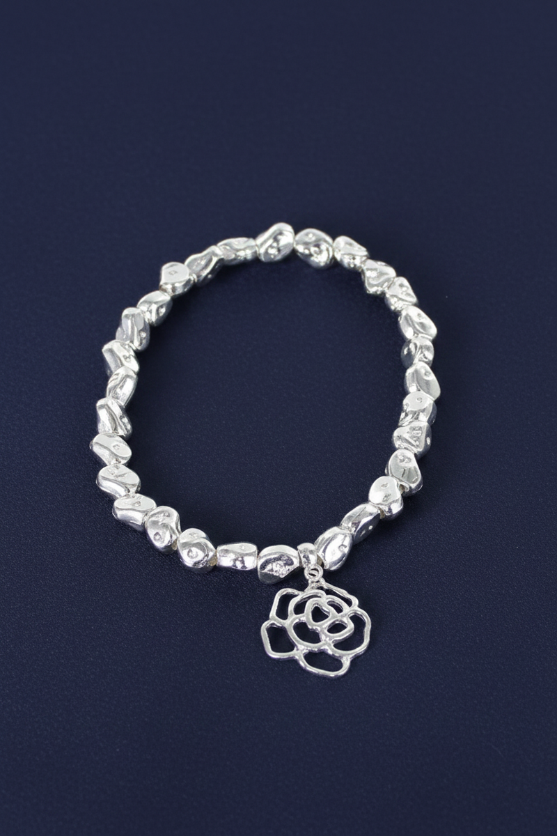 Silver plated nugget bead elasticated bracelet with an open rose charm with layered petal detail on a deep navy blue background