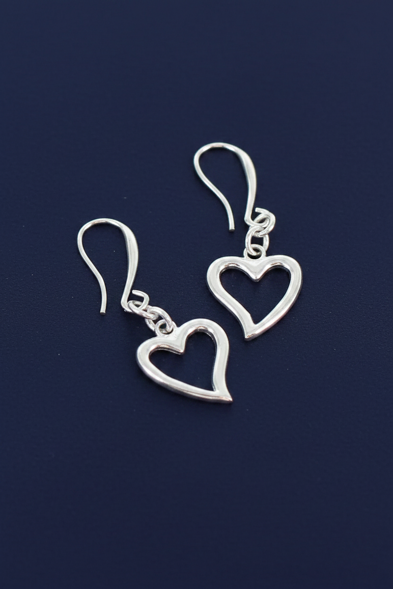 Silver plated open heart charm earrings on short chain with hook fittings on a deep navy blue background