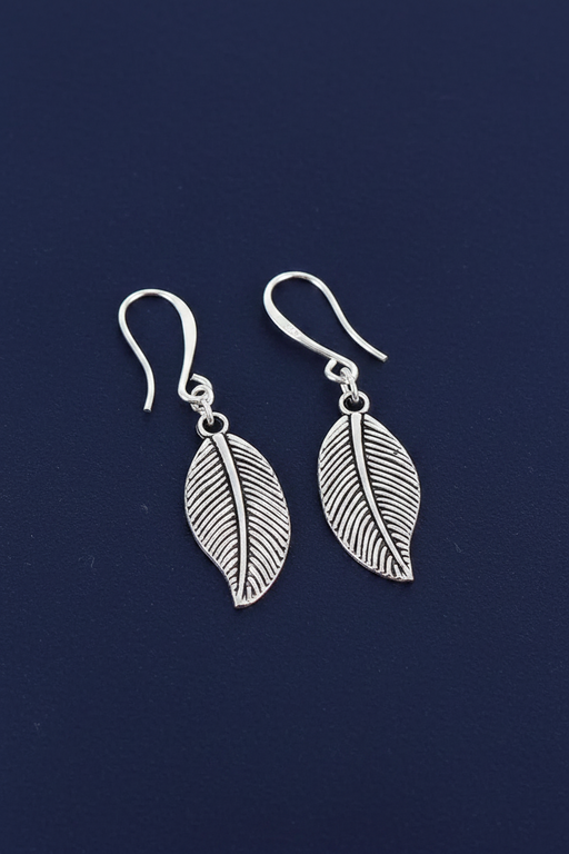 Silver plated leaf charm drop earrings with fine vein texture on hook fittings on a deep navy blue background
