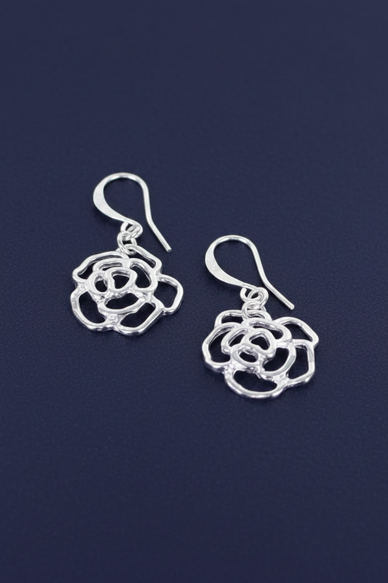 Silver plated open rose charm drop earrings with layered petal detail on hook fittings on a deep navy blue background