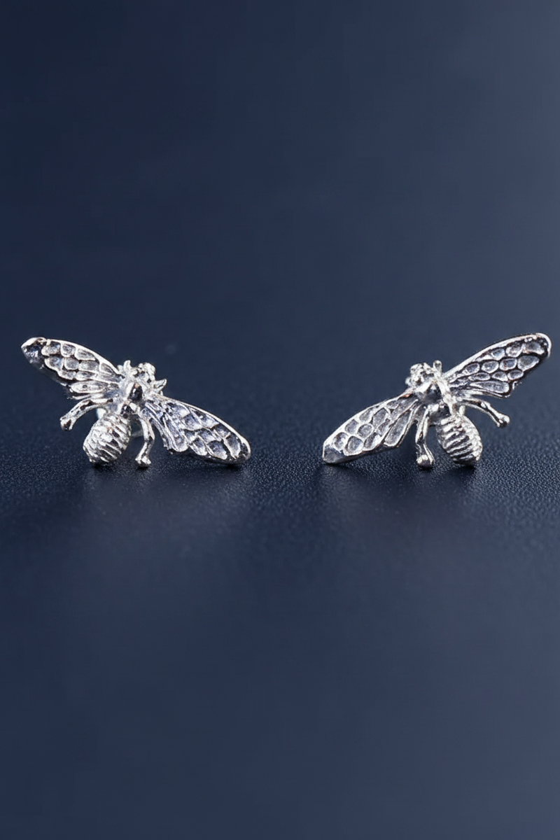 Silver plated bumble bee stud earrings with detailed textured wings and body on a deep navy blue background