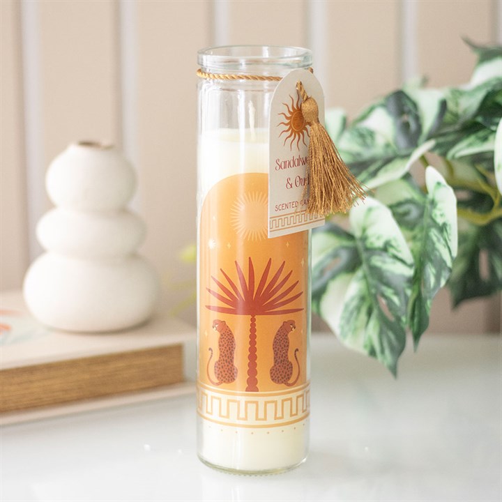 Leopard Palm Sandalwood & Oud tube candle in glass jar with gold tassel and gift tag, styled on a white surface with a plant and vase in the background