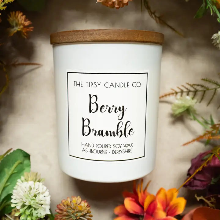 Tipsy Berry Bramble Scented Candle in white matte glass jar with wooden lid surrounded by autumn flowers and foliage