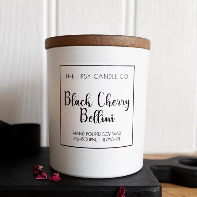 Tipsy Black Cherry Bellini Scented Candle in white matte glass jar with wooden lid on dark slate surface