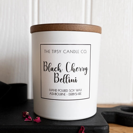 Tipsy Black Cherry Bellini Scented Candle in white matte glass jar with wooden lid on dark slate surface