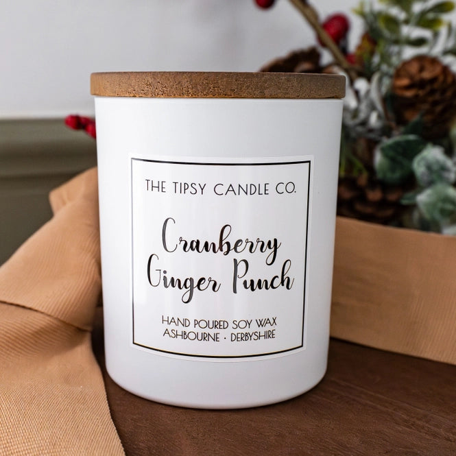Tipsy Cranberry Ginger Punch Scented Candle in white matte glass jar with wooden lid styled with pine cones and red berries