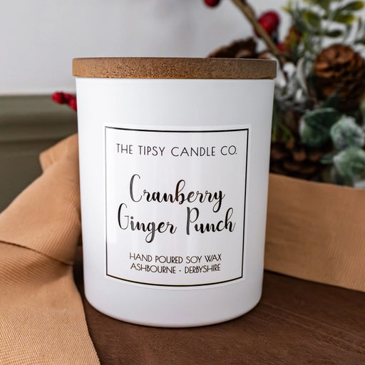 Tipsy Cranberry Ginger Punch Scented Candle in white matte glass jar with wooden lid styled with pine cones and red berries