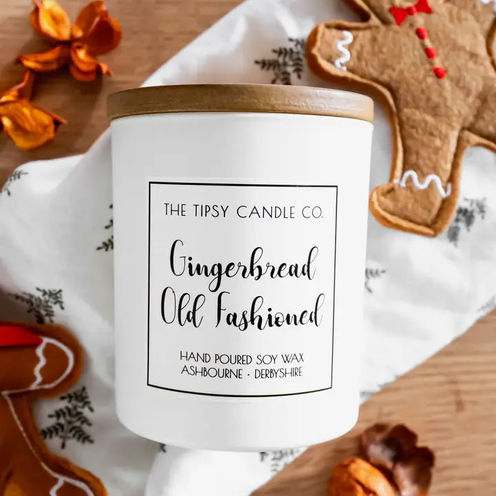 Tipsy Gingerbread Old Fashioned Scented Candle in white matte glass jar with wooden lid styled with gingerbread men on festive linen