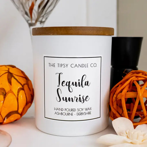 Tipsy Tequila Sunrise Scented Candle in white matte glass jar with wooden lid styled with orange decorative ornaments