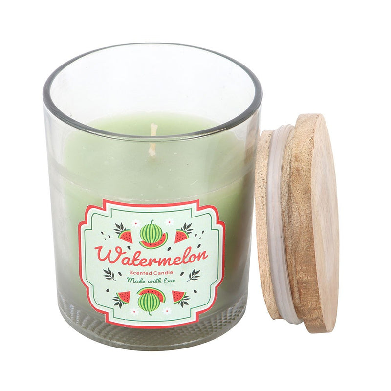 Watermelon Scented Candle, close-up of clear glass jar with wooden lid removed showing candle wax and watermelon illustrated label, white background
