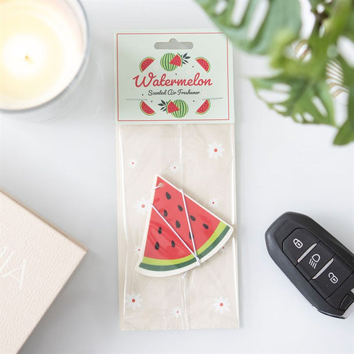 Watermelon Scented Air Freshener in clear packaging with illustrated watermelon header card on a white surface beside a car key and candle