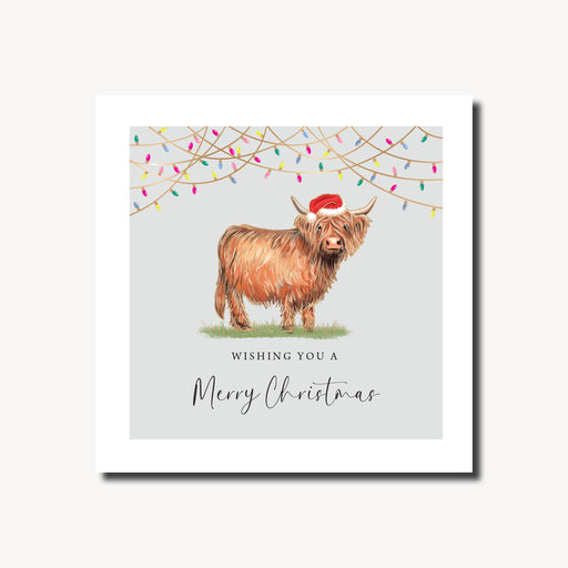 Merry Christmas card featuring a fluffy Highland cow in a Santa hat standing beneath strings of colourful fairy lights on a soft grey background, foil finish, 155 x 155mm
