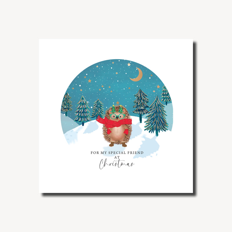 Christmas card for a special friend featuring a cosy hedgehog in a red scarf and Christmas tree glasses in a snowy winter scene with dark fir trees and a teal night sky, gold foil finish, 155 x 155mm