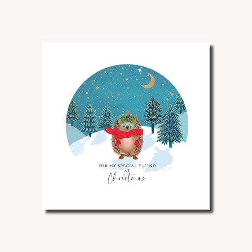 Christmas card for a special friend featuring a cosy hedgehog in a red scarf and Christmas tree glasses in a snowy winter scene with dark fir trees and a teal night sky, gold foil finish, 155 x 155mm