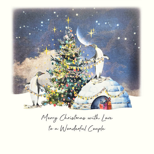 An illustrated Christmas card showing two penguins decorating a glittering Christmas tree beside an igloo under a starry night sky with a crescent moon, with hand painted glitter detail and the sentiment "Merry Christmas with Love to a Wonderful Couple"