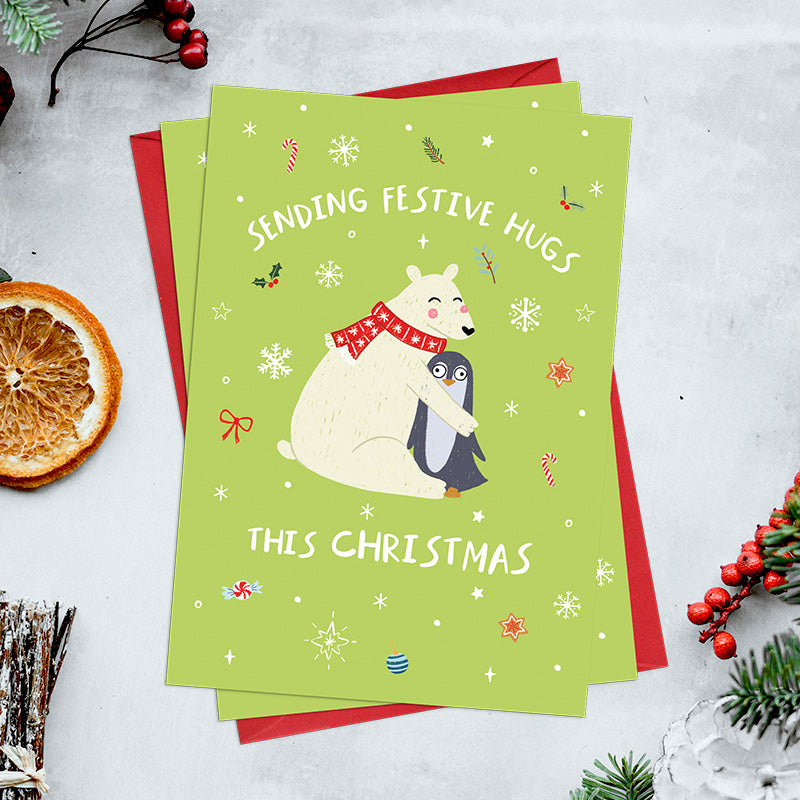 Pack of 6 Sending Festive Hugs Christmas cards featuring a polar bear wrapped up in a warm scarf hugging a penguin, surrounded by festive illustrations