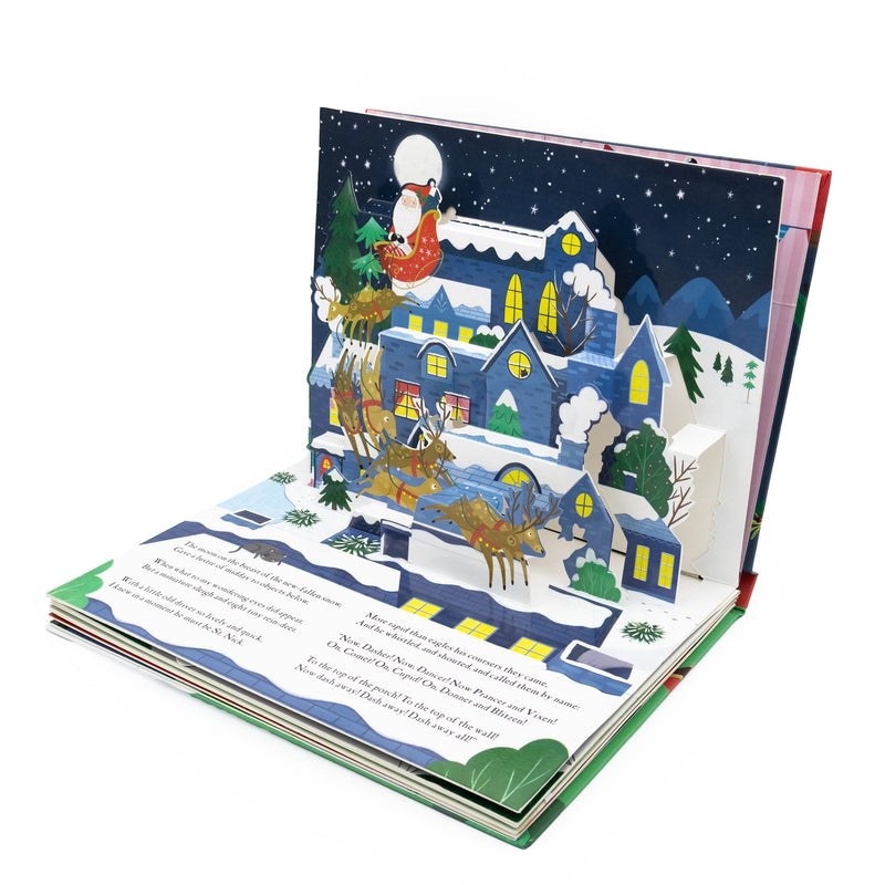 The Night Before Christmas Pop-Up Book open spread showing Santa in his sleigh pulled by reindeer flying over a snowy village in a 3D pop-up night scene