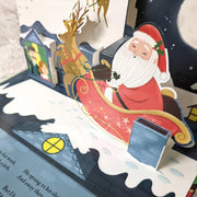 The Night Before Christmas Pop-Up Book open spread close-up of Santa seated in his sleigh with a reindeer beside a snow-covered rooftop pop-up scene