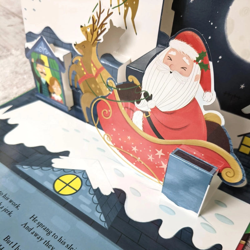 The Night Before Christmas Pop-Up Book open spread close-up of Santa seated in his sleigh with a reindeer beside a snow-covered rooftop pop-up scene