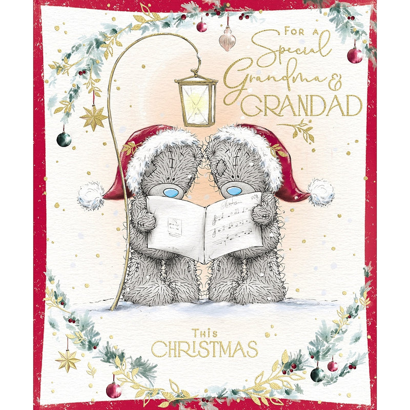 Special Grandma and Grandad Tatty Teddy Christmas card featuring two bears wearing Santa hats and singing from a songbook beneath a lantern, framed by festive foliage, baubles and stars.